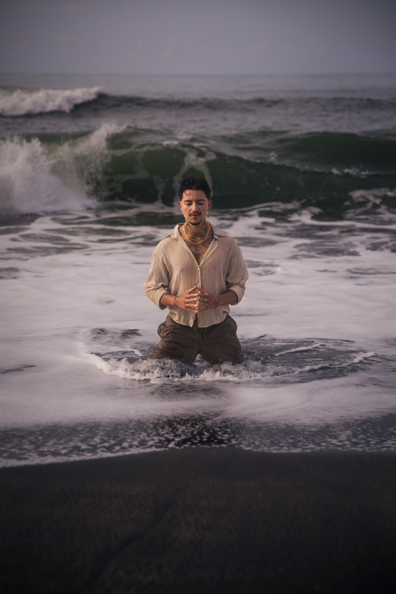 A man kneeling in meditation among ocean waves at dusk